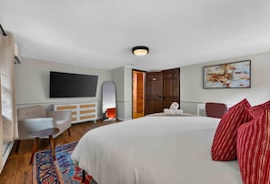 Ein Hotelzimmer mit einem großen Bett, einem Flachbildfernseher, einer Sitzecke, einem kleinen Tisch und einem dekorativen Teppich.