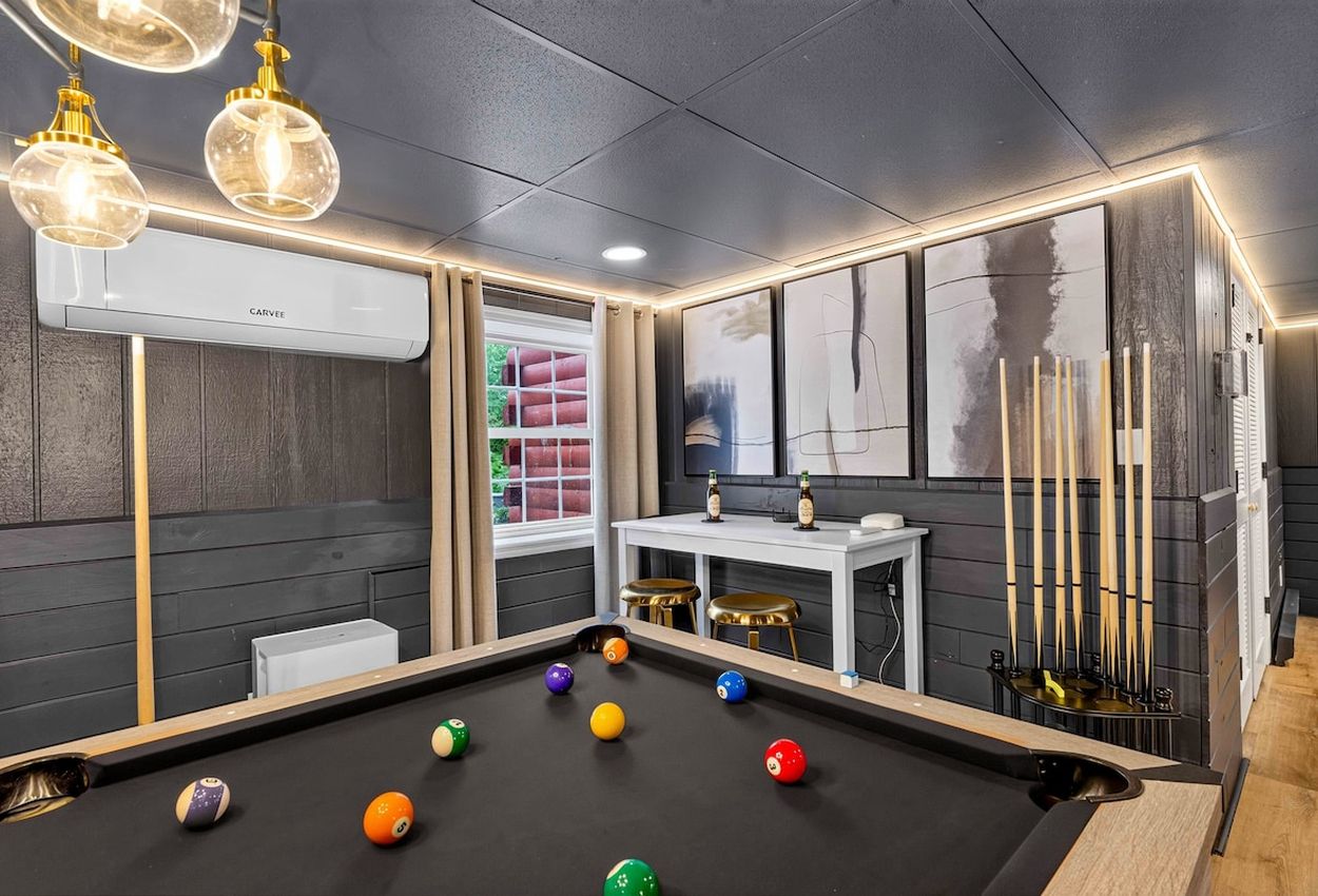 A billiards room with a pool table, cue sticks, and a white table with bottles.