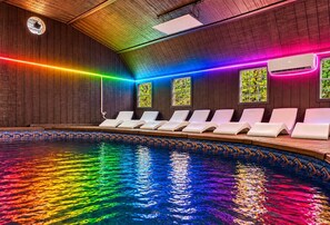 Ein Schwimmbecken mit einer farbigen Lichtleiste, Liegestühlen und einer Holzbeschichtung.