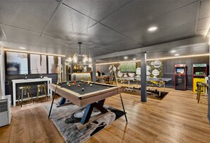 Ein moderner, überdachter Freizeitbereich mit Billardtisch, Barhocker und Spielautomaten.