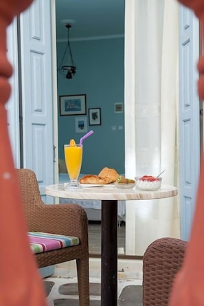 A dining area with a table set for breakfast, including a glass of orange juice, croissants, and a bowl of fruit. - Seven Brothers Htl (Poros)