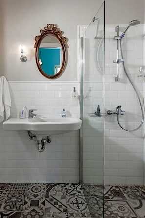 A bathroom with a white sink, a mirror, a shower, and patterned floor tiles. - Seven Brothers Htl (Poros)