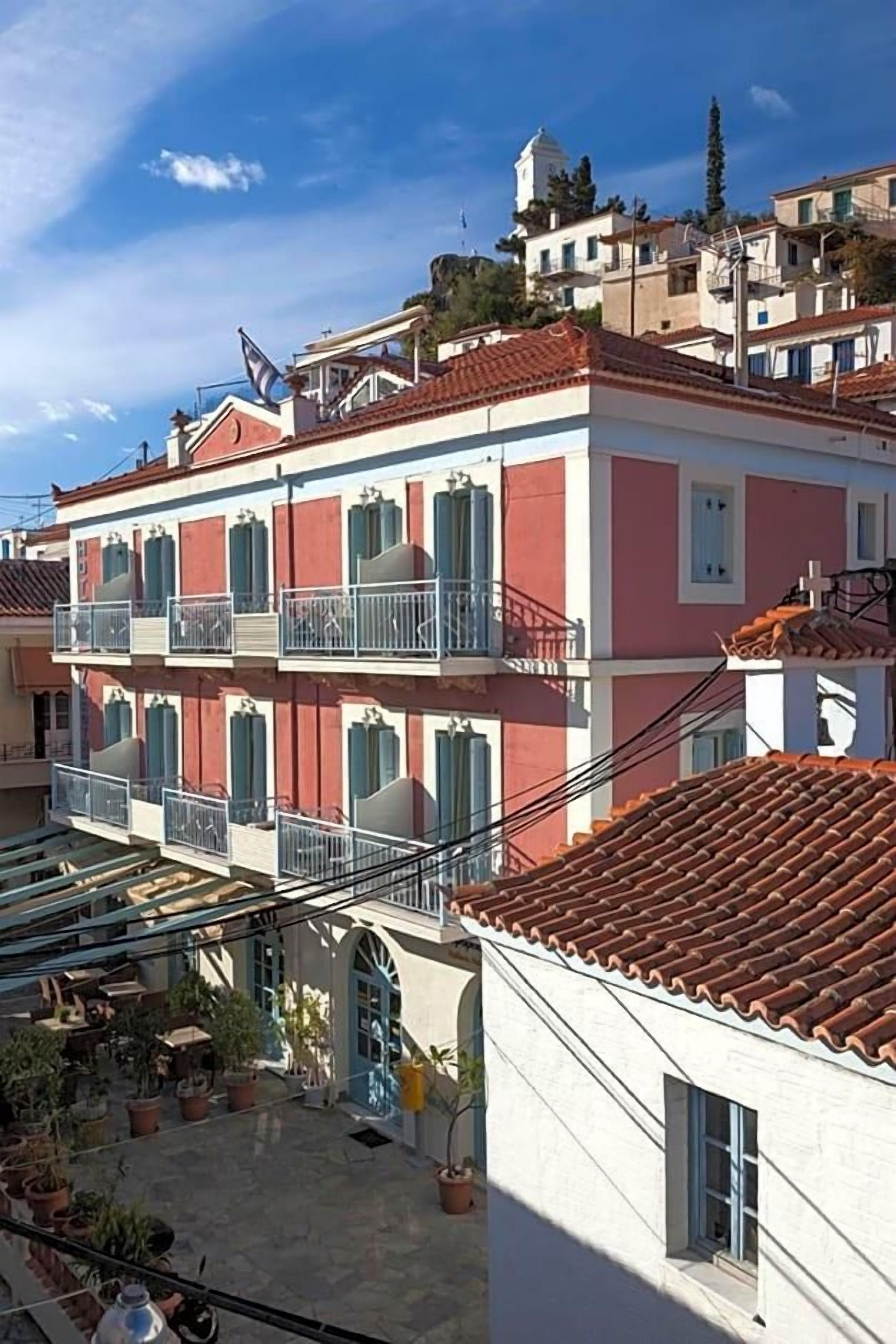 Un edificio de varios pisos con balcones, techo de tejas y un patio con plantas en macetas.