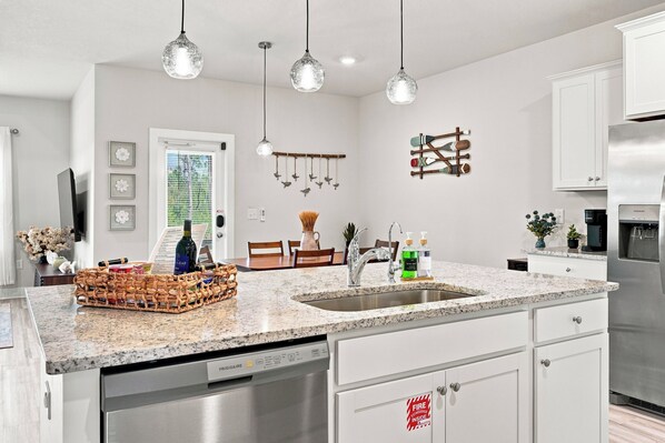 A modern kitchen with a granite countertop, stainless steel appliances, and pendant lighting.