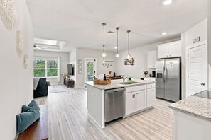 A modern kitchen with a central island, stainless steel appliances, pendant lighting, and a view of the outdoors.