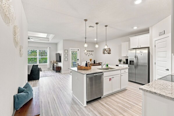 A modern kitchen with a central island, stainless steel appliances, pendant lighting, and a view of the outdoors.