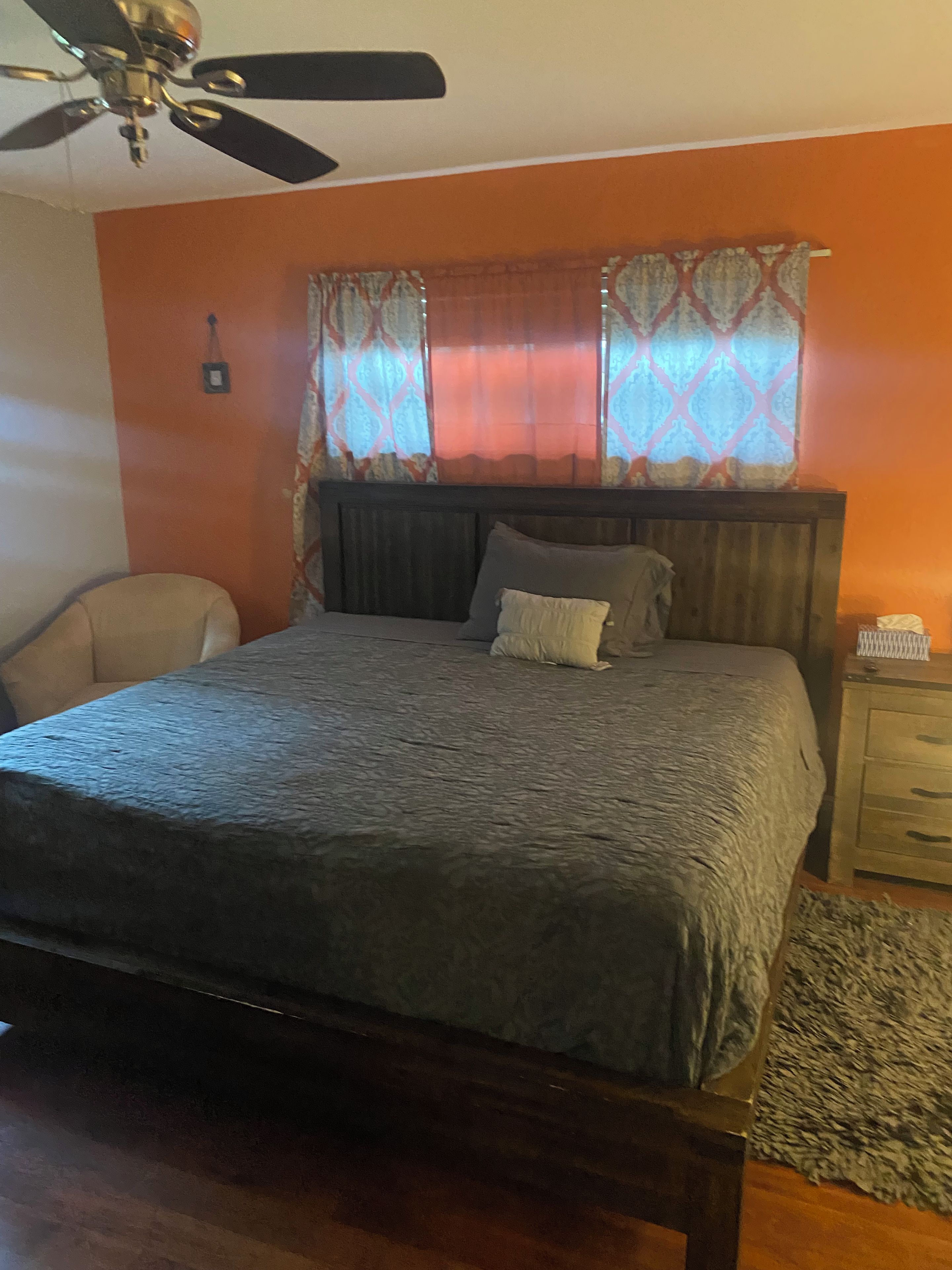 Un dormitorio con una cama, una silla, una mesita de noche y un ventilador de techo.