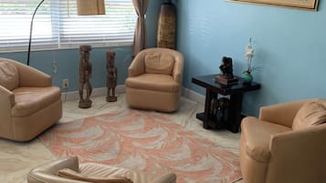 Una sala de estar con pared azul, un ventanal con persianas, una lámpara de pie y tres sillones color beige.