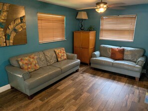 A living room with two sofas, wooden flooring, and a ceiling fan.