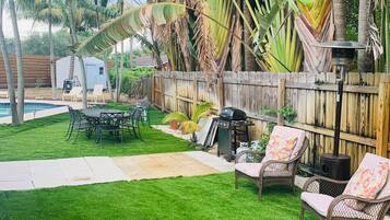 A backyard with a grassy lawn, a barbecue grill, wicker furniture, and a wooden fence.
