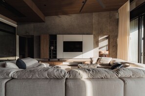 Ein modernes Wohnzimmer mit einem Ecksofa, einem Flachbildfernseher und einer Holzbalkendecke.