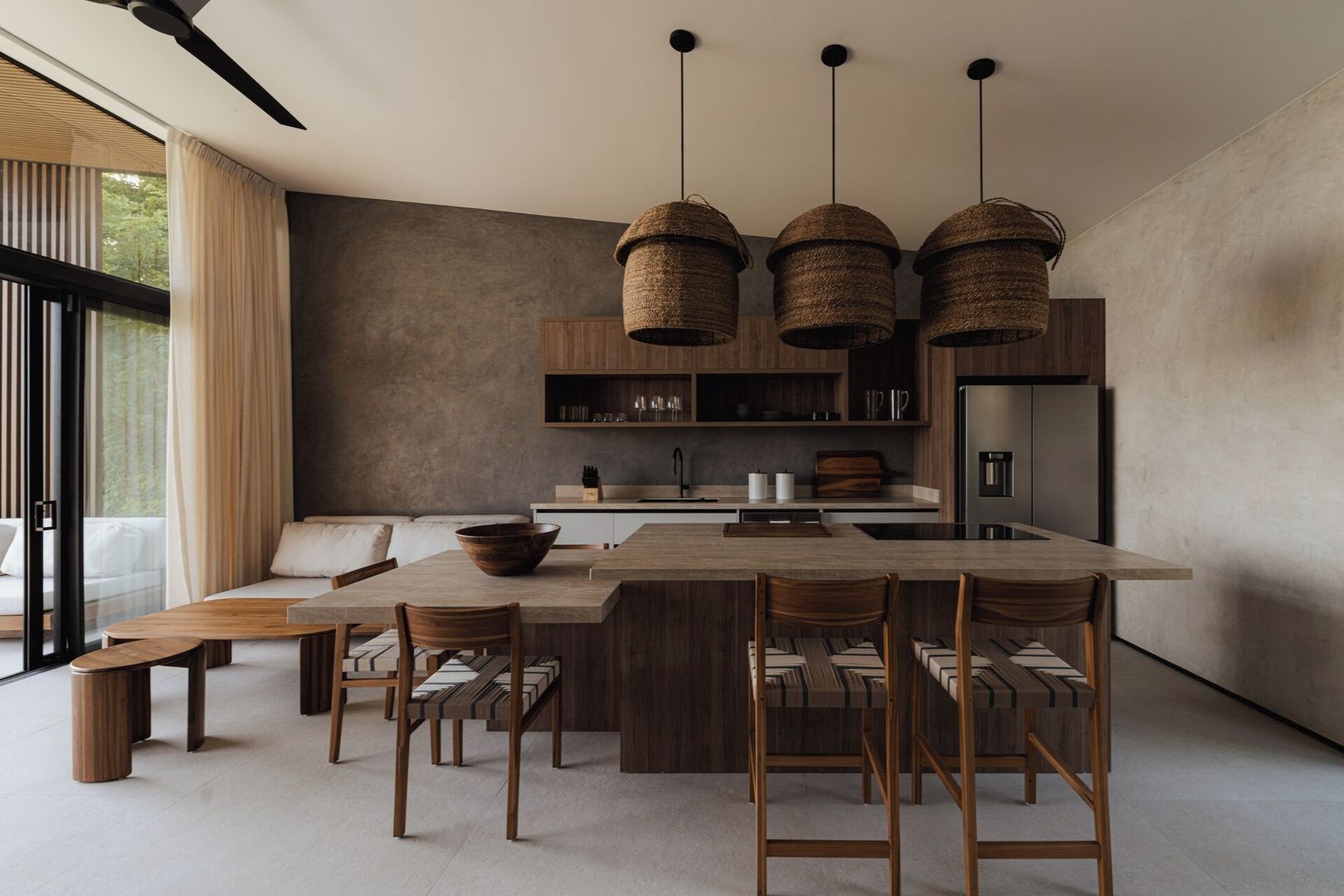 A modern kitchen with a central island, wooden chairs, and hanging baskets.