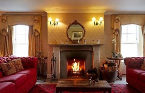 Ein traditionell eingerichteter Raum mit Kamin, zwei roten Sofas und einem Spiegel über dem Kaminvorsatz.