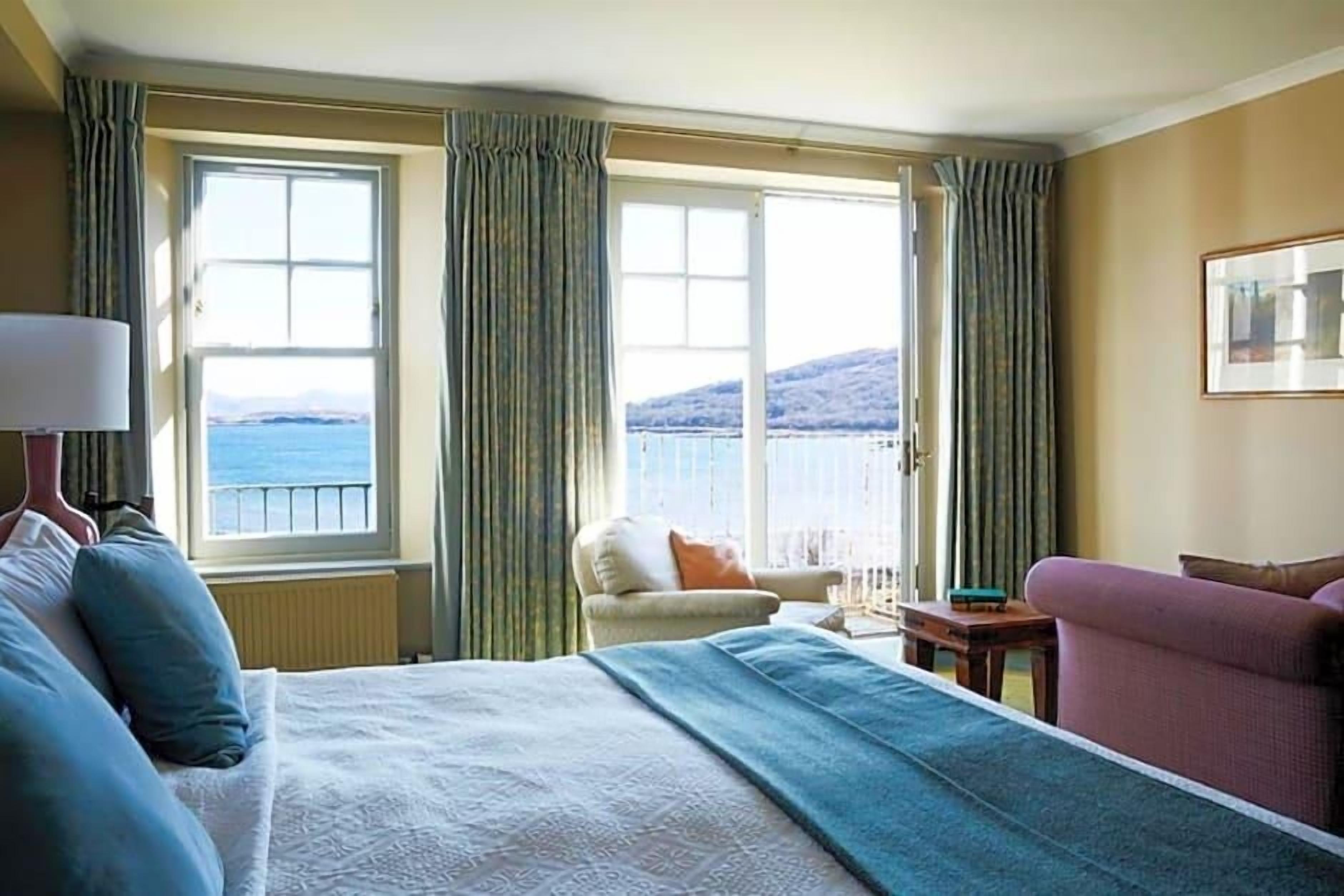 A hotel room with a bed, a chair, a table, and a view of the sea.