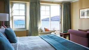 A hotel room with a bed, a chair, a table, and a view of the sea. - Kinloch Lodge (Sleat)