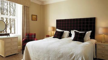 Una habitación de hotel con una cama grande, un tocador, una silla y una mesita de noche con una lámpara.