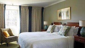 A hotel room with a large bed, two bedside tables, a chair, and a window with curtains. - Kinloch Lodge (Sleat)
