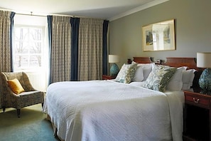 A hotel room with a large bed, two bedside tables, a chair, and a window with curtains. - Kinloch Lodge (Sleat)