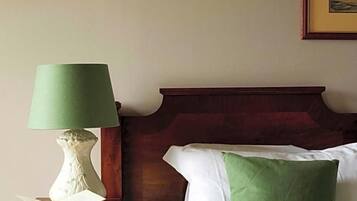 Ein ordentlich gemachtes Bett mit einem grünen Kopfkissen, ein Nachttisch mit einer Lampe und ein gerahmtes Bild an der Wand.