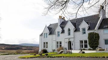 A large, white, two-story house with a symmetrical facade, multiple chimneys, and a well-maintained lawn.