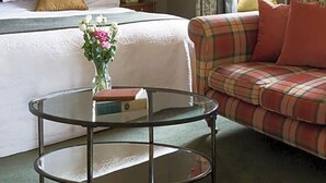 A hotel room with a bed, a sofa, a round glass table, and a framed picture on the wall. - Kinloch Lodge (Sleat)