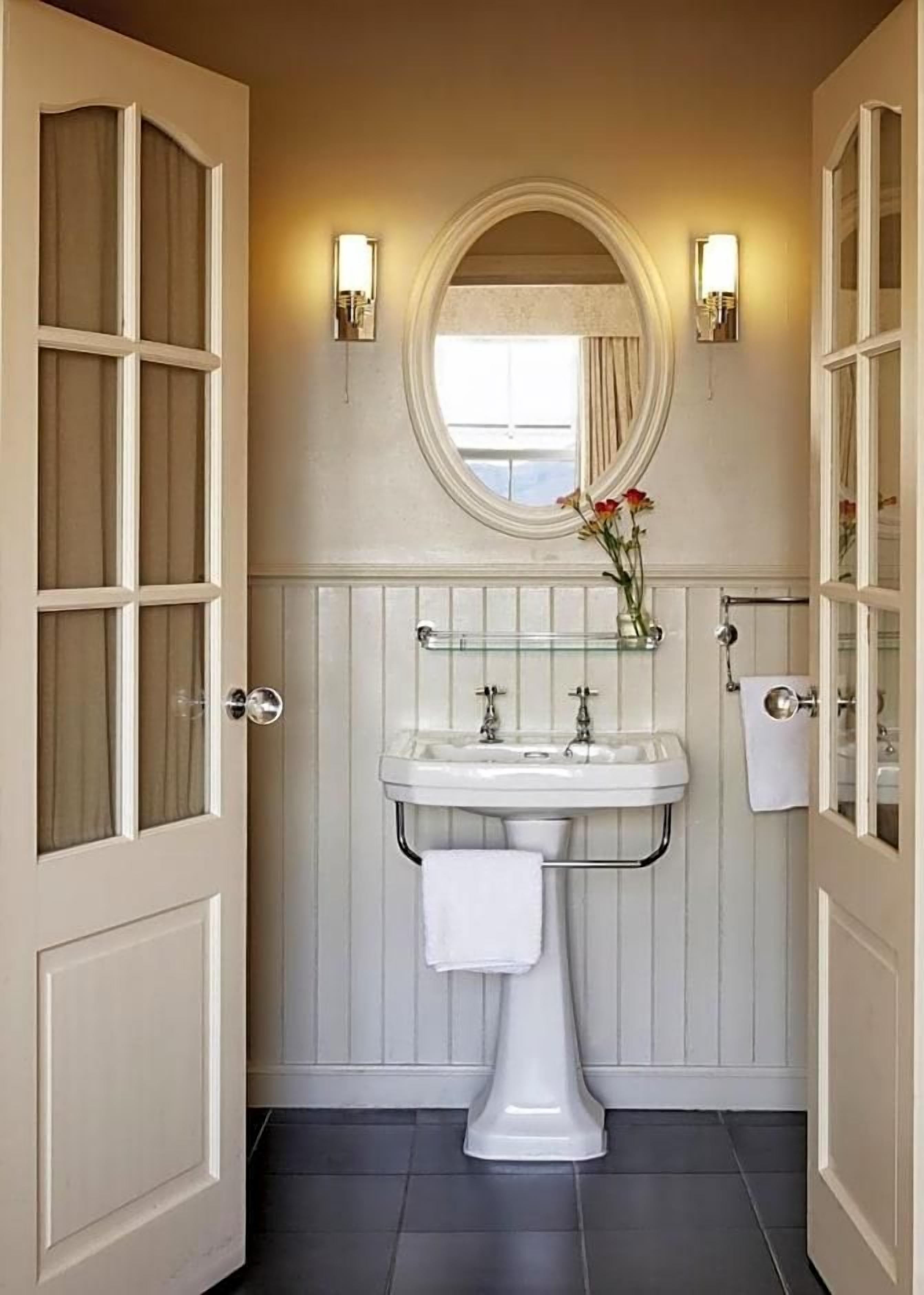 Un baño con lavamanos pedestal, espejo y ventana con cortinas.