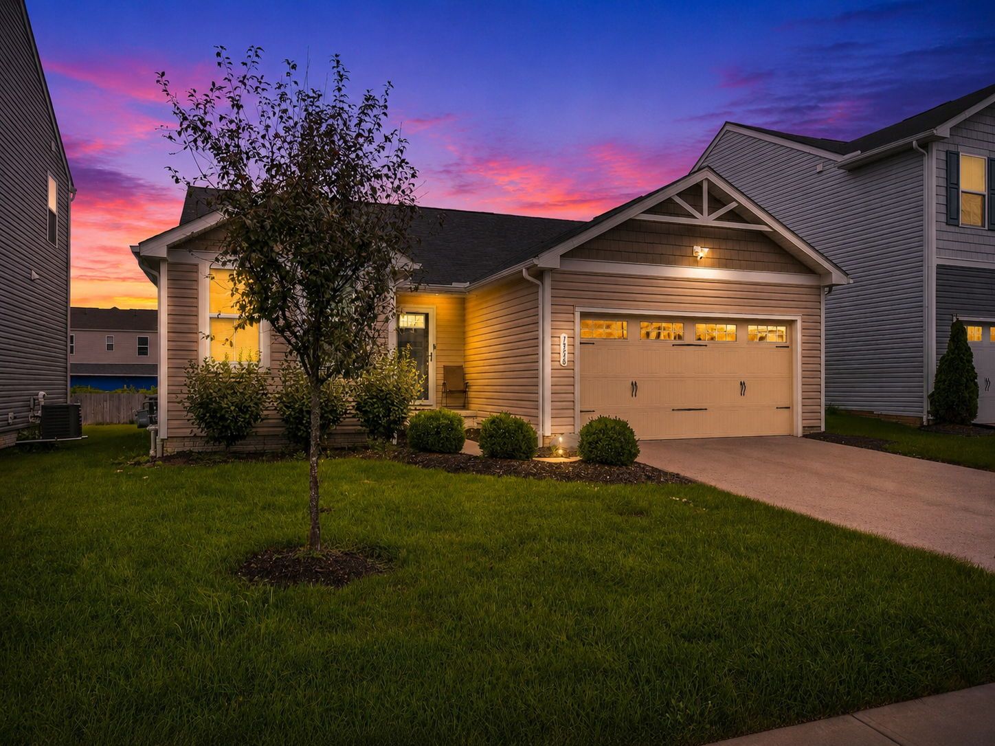 A two-story residential building with a garage, a well-maintained lawn, and a tree in the front yard.