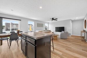 Een moderne keuken met een groot eiland, een eetgedeelte met stoelen, een flatscreen televisie en een plafondventilator.