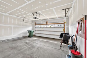 A garage with a concrete floor, a green trash bin, and a tool rack with various tools. - Beautiful 3-bedroom house pleasant Grove City (Grove City)