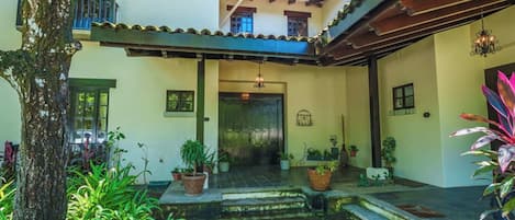 A courtyard with a covered seating area, potted plants, and a tree.