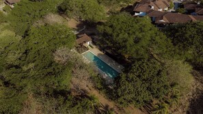 An aerial view of a residential area with a swimming pool surrounded by dense vegetation and houses with brown roofs. - Modern 4BR Villa, All En-Suite · Hacienda Pinilla (Guanacaste)