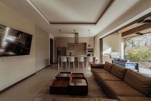 A modern living room with a sofa, a coffee table, and a TV mounted on the wall. - Modern 4BR Villa, All En-Suite · Hacienda Pinilla (Guanacaste)