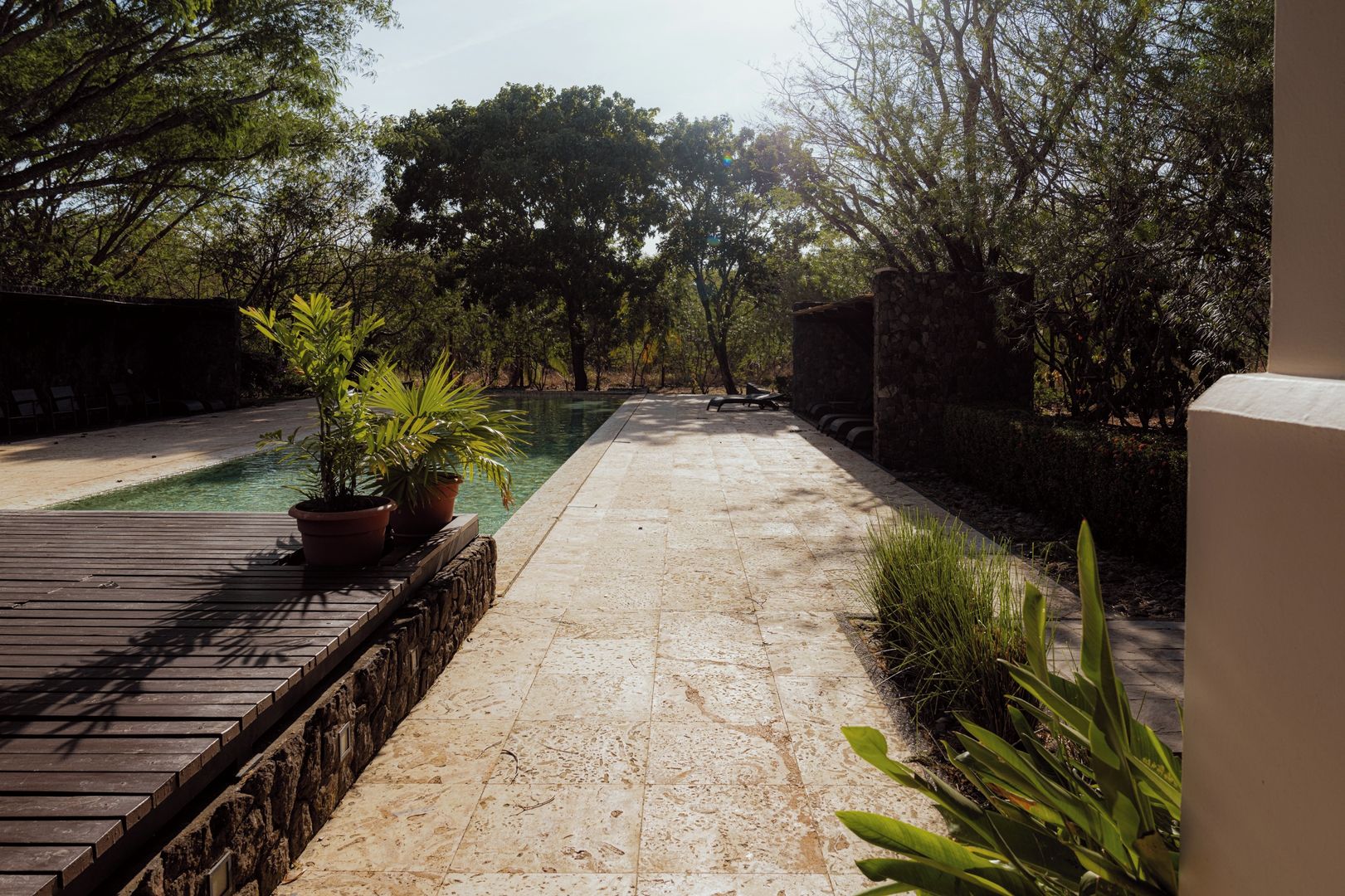 A pool area with a wooden deck and potted plants.