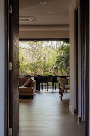 A corridor leading to a dining area with a view of a garden. - Modern 4BR Villa, All En-Suite · Hacienda Pinilla (Guanacaste)