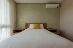 A hotel room with a large bed, wooden headboard, two bedside tables, and a wall-mounted air conditioner. - Modern 4BR Villa, All En-Suite · Hacienda Pinilla (Guanacaste)