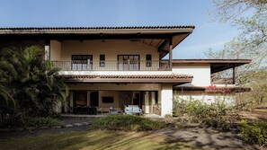 Une maison à deux étages dotée d’un balcon, d’une terrasse avec des meubles d’extérieur et d’un jardin où poussent différentes espèces de plantes.