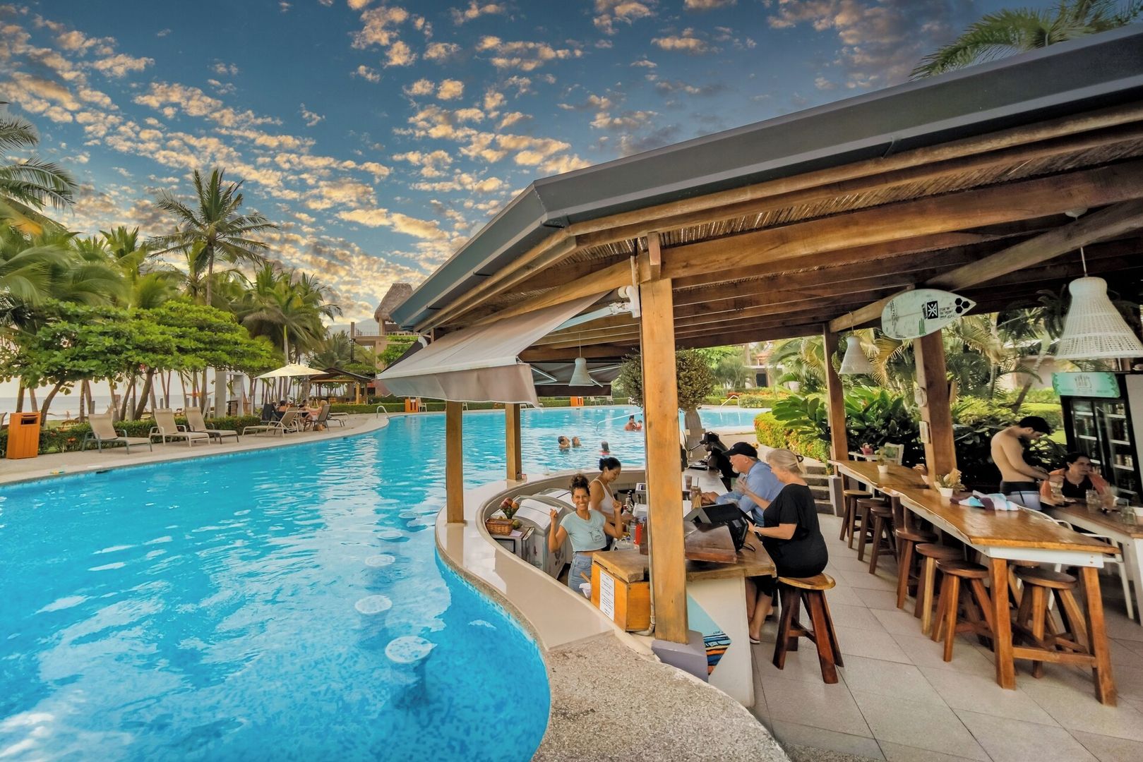 A poolside bar area with a pool, lounge chairs, and a covered seating area.
