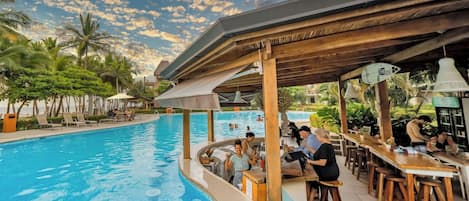 A poolside bar area with a pool, lounge chairs, and a covered seating area.