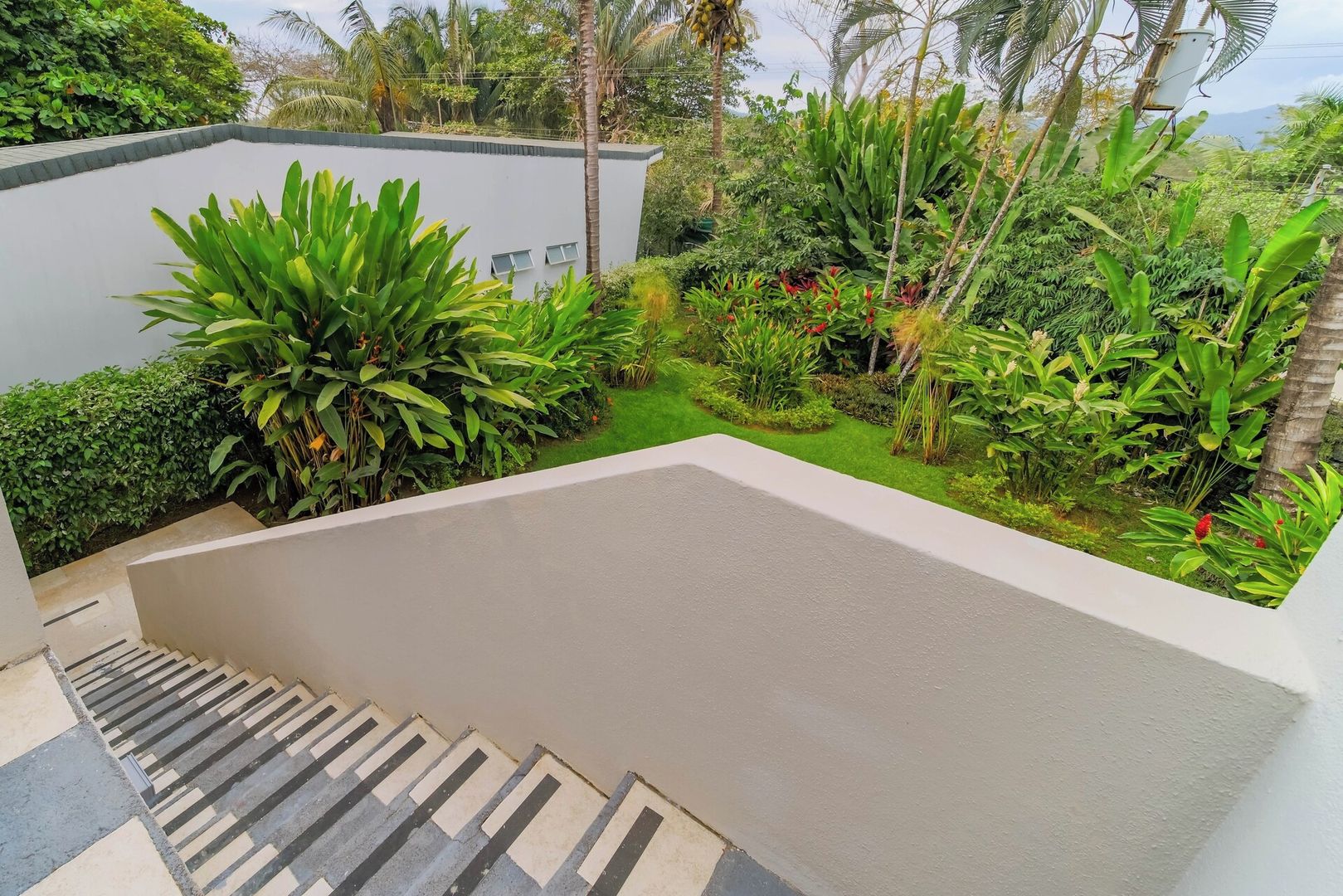 A modern building with a flat roof, surrounded by lush greenery and a clear sky.