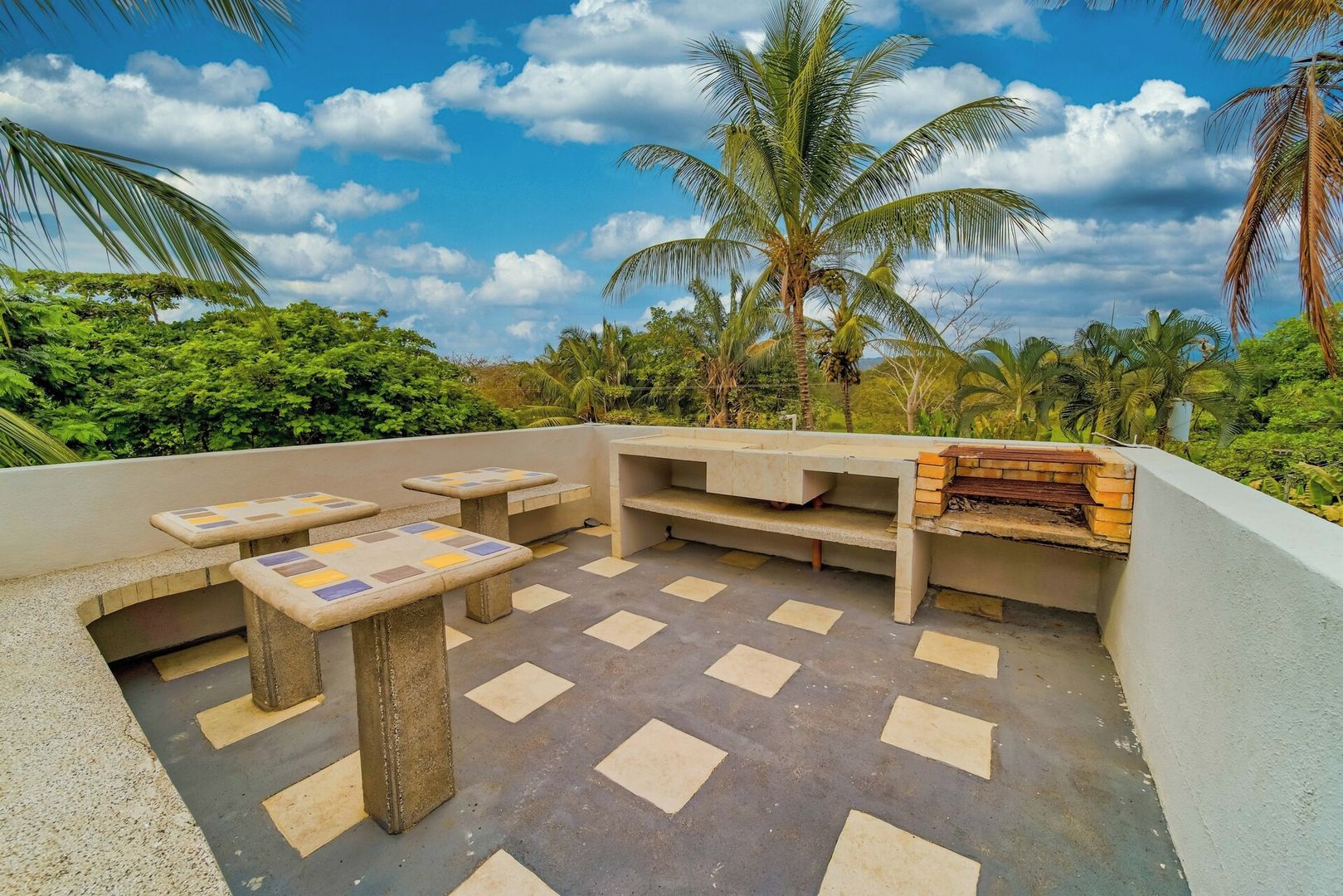 An outdoor patio with seating and a barbecue area, surrounded by lush greenery and palm trees.