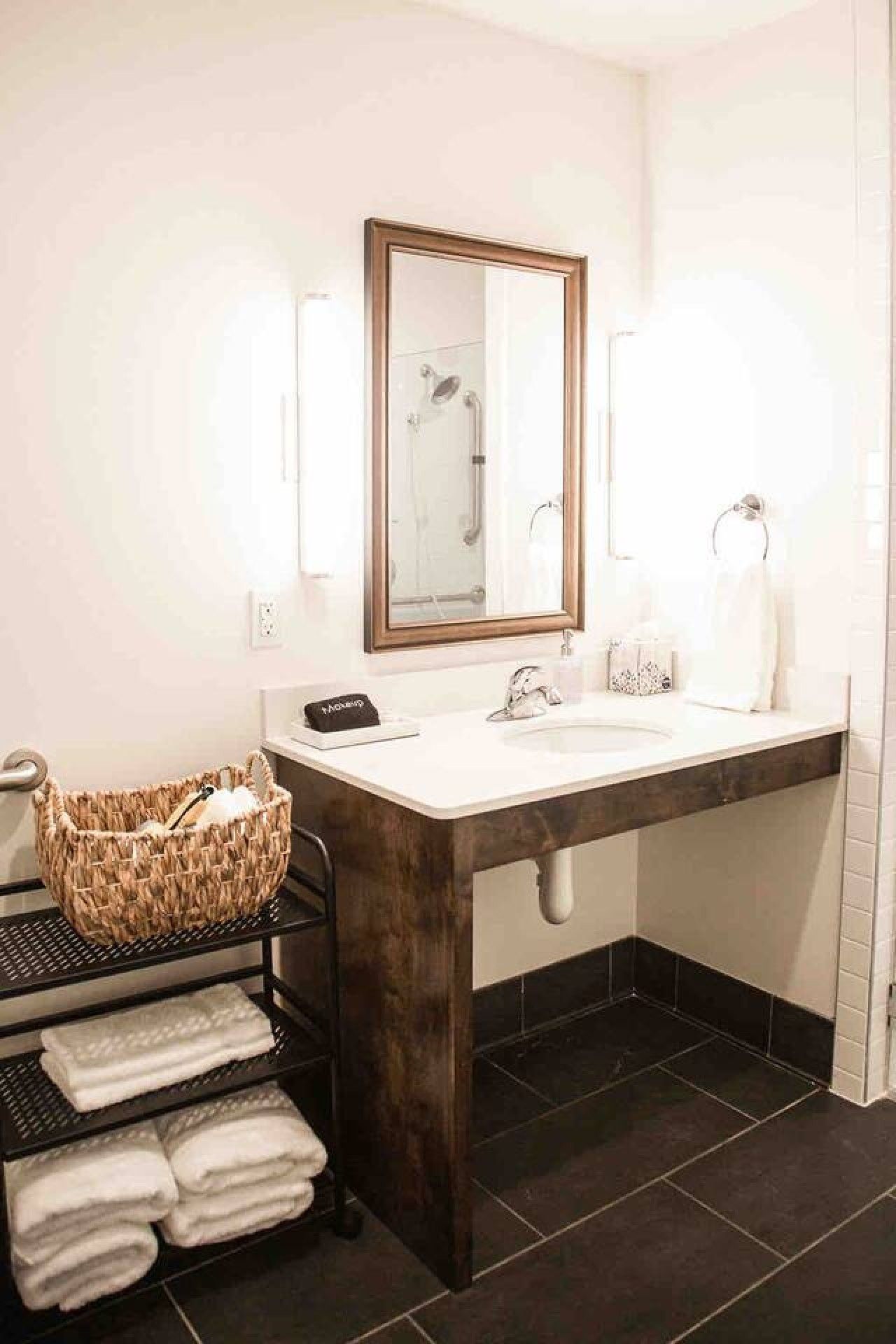 Un baño con un espejo grande, un lavabo, un perchero para toallas y una cesta.
