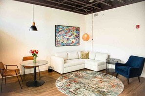 Una sala de estar moderna con un sofá blanco, una mesa de centro redonda, un sillón azul, una mesita redonda y un cuadro abstracto colorido en la pared.