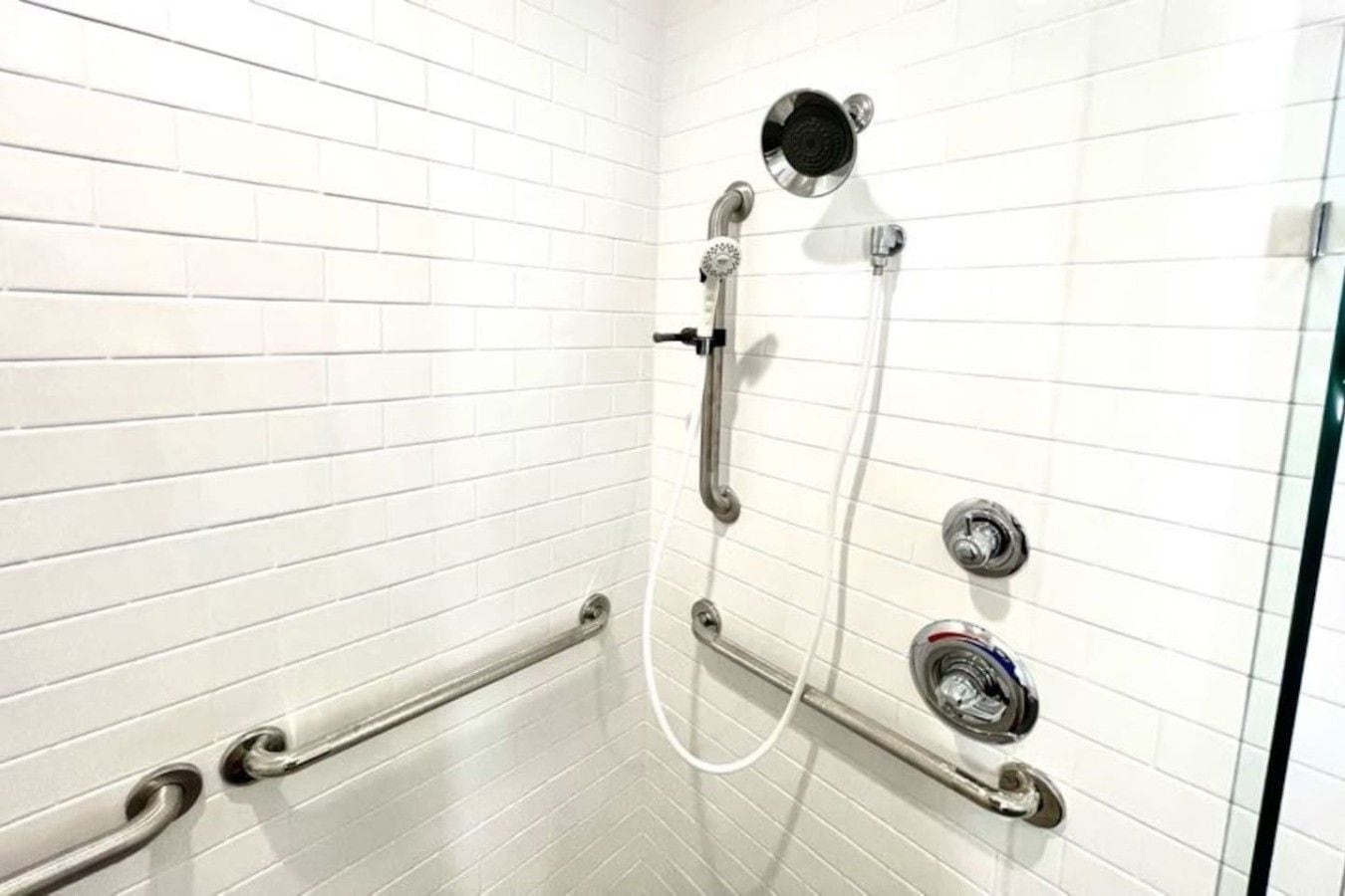 A shower with a handheld showerhead, a wall-mounted faucet, and a handheld shower control.