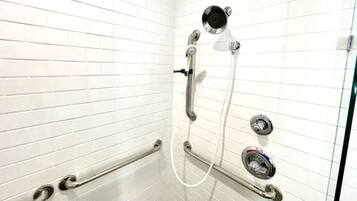 A shower with a handheld showerhead, a wall-mounted faucet, and a handheld shower control.