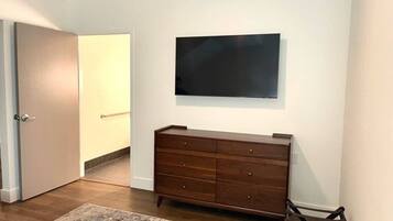 A room with a wooden dresser, a flat-screen TV mounted on the wall, a door, and a rug on the floor.