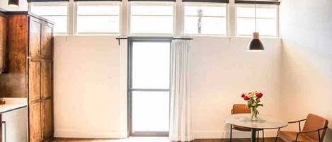 Una habitación con un ventanal amplio, una mesa redonda con sillas y un armario de madera.