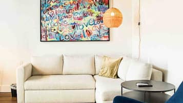 Un salon moderne avec un canapé, un fauteuil bleu, une table basse ronde, un tapis coloré et une peinture abstraite aux couleurs vives accrochée au mur.