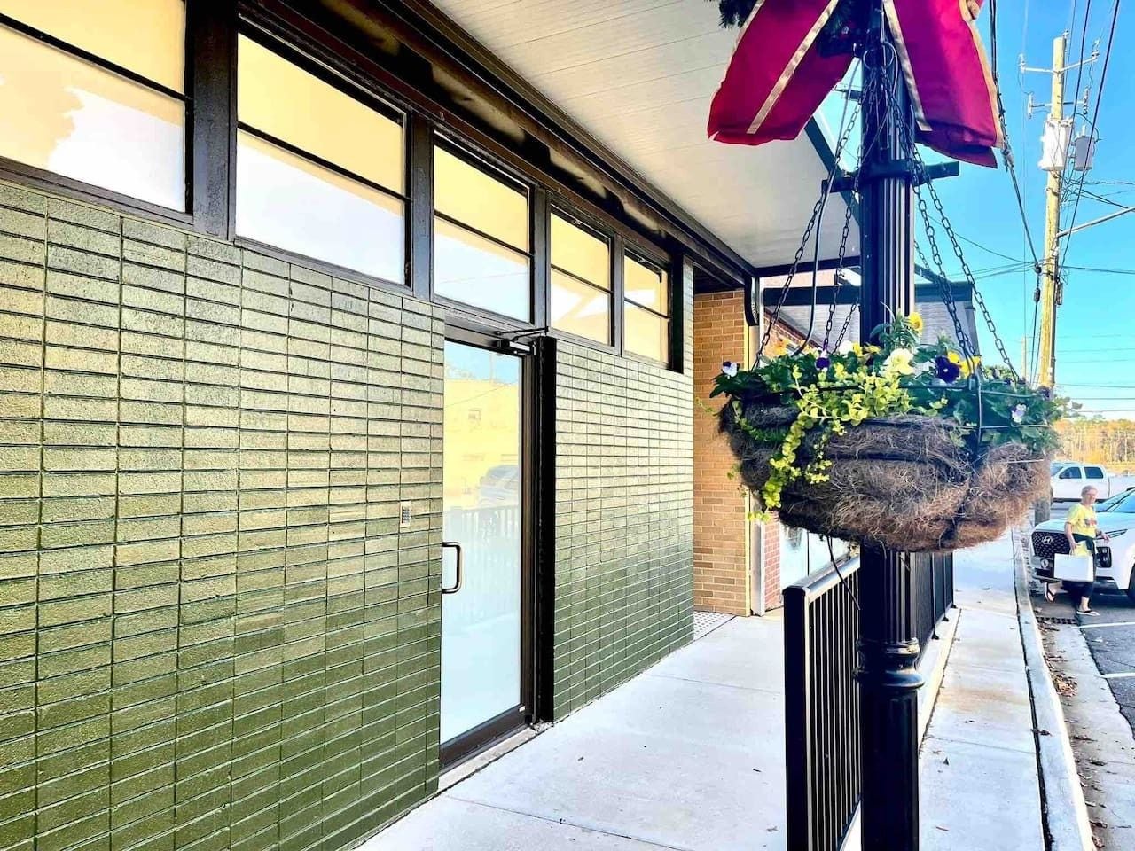 A building with a brick facade, a glass door entrance, and a hanging planter with flowers.