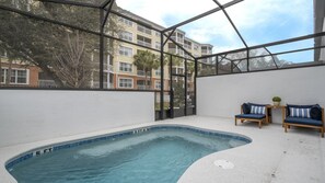 An indoor swimming pool with a glass enclosure, a small seating area with two chairs, and a view of a multi-story building in the background. - 5BR Luxury Townhouse with Pool at Paradiso Grande (Orlando)
