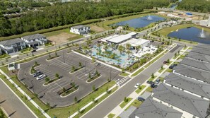 A large parking lot with multiple rows of parking spaces, a swimming pool area with lounge chairs, and a building with a flat roof. - 5BR Luxury Townhouse with Pool at Paradiso Grande (Orlando)